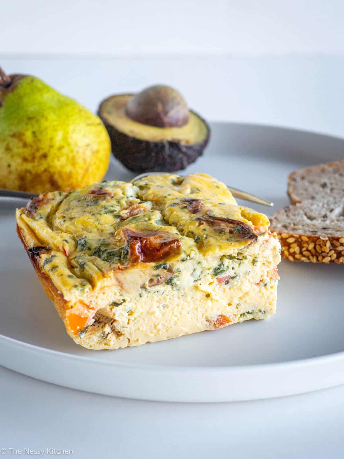 Breakfast casserole on a plate with avocado, fruit and toast.