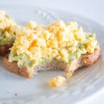Scrambled eggs and avocado on toast with a bite take out.