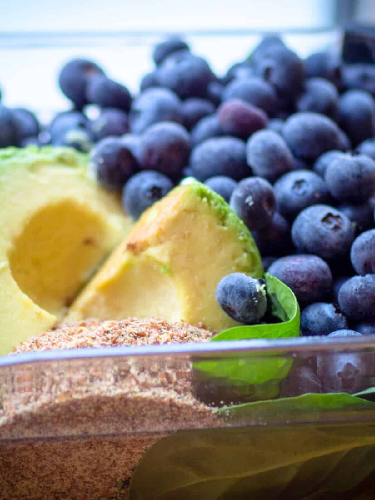 Spinach and avocado in a blender with blueberries.