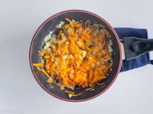 Sautéed carrots and onions in a frying pan.