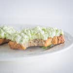 Toast topped with avocado and cottage cheese with a bite taken out.