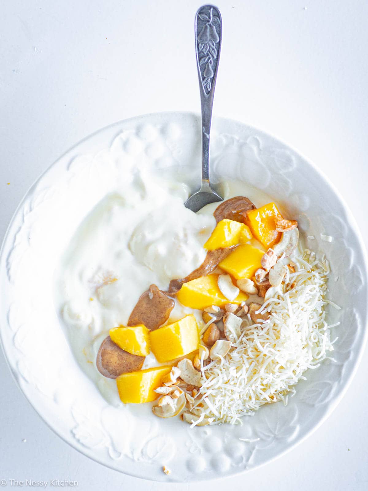 Bowl of yogurt topped with mango and nuts.