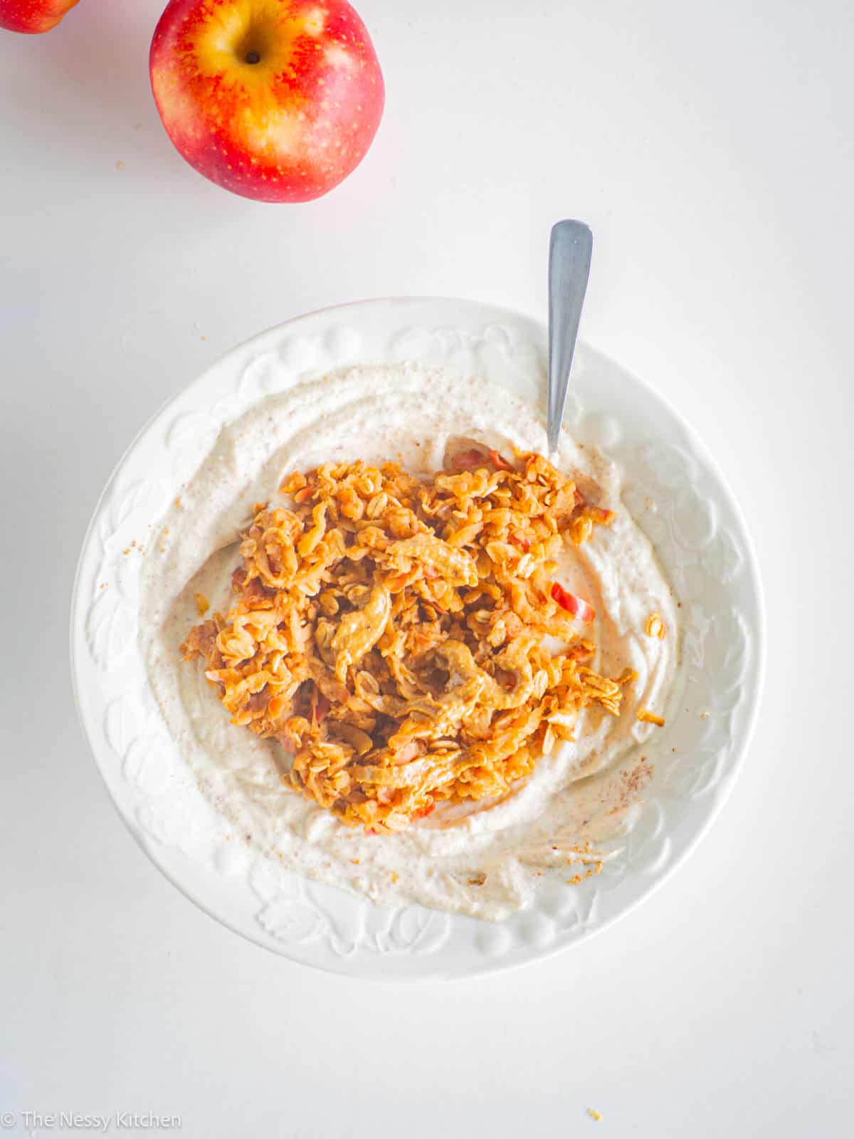 Apple yogurt bowl with spoon and apples on counter.