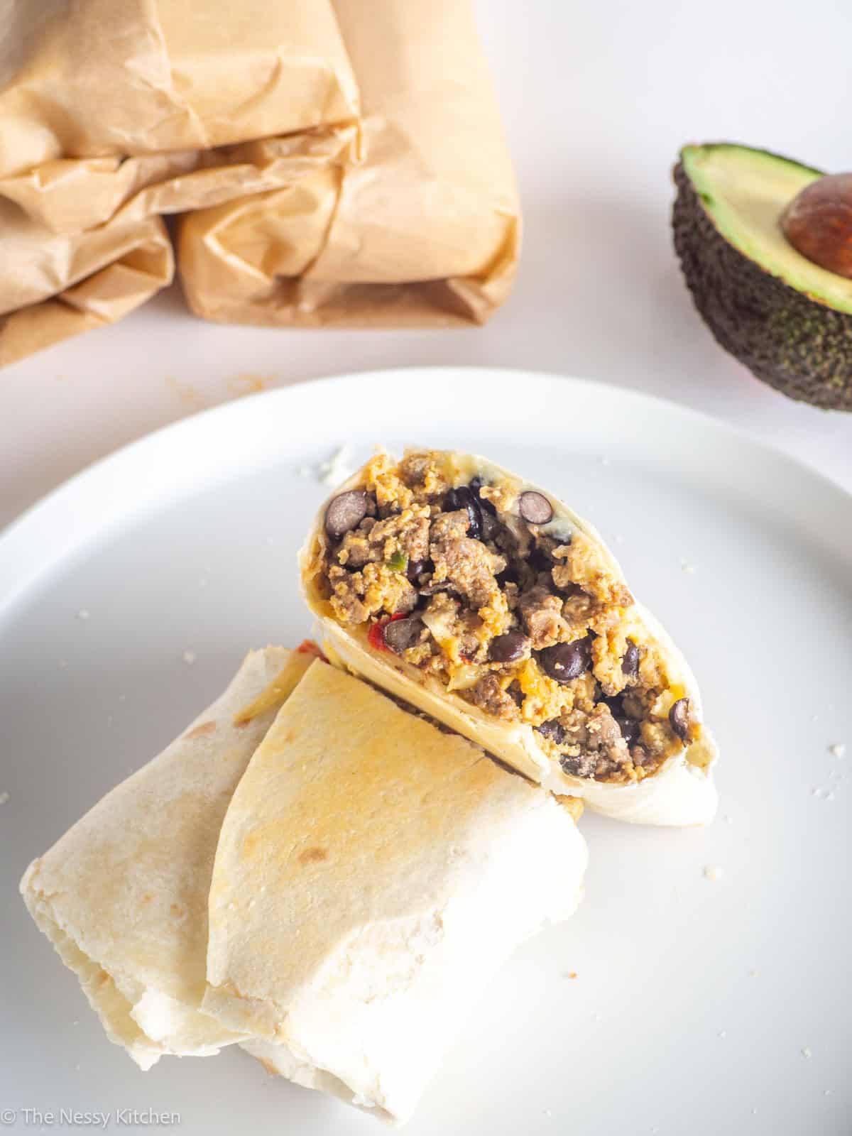Breakfast burrito cut in half on plate with stack and avocado.