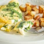 Omelet and potatoes on plate with piece in fork.