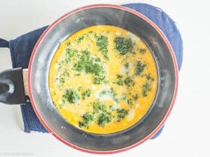 Beaten eggs over spinach in pan.