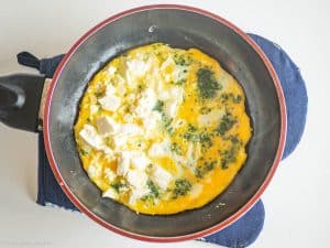 Feta on one half of the omelet in the pan.