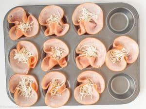 Cheese sprinkled on top of ham slices.
