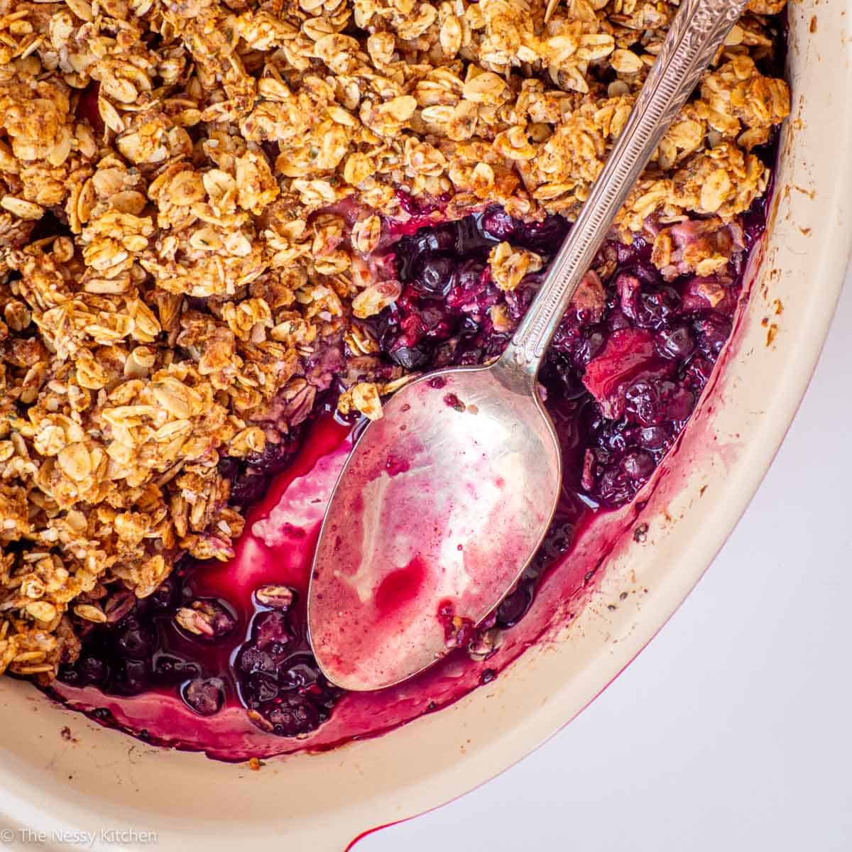 Spoon in a baking dish with berry crisp.