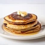 Stack of pancakes on a plate with maple syrup and butter.