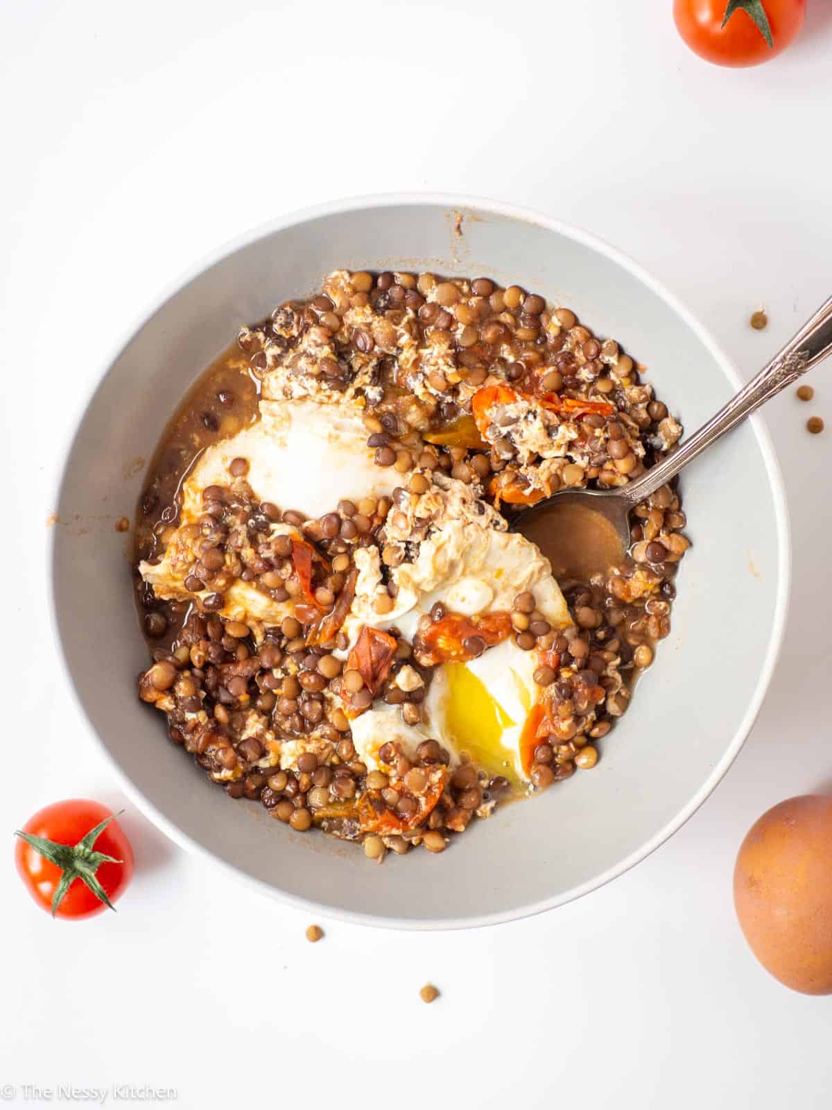 Lentil and egg breakfast bowl plated with tomatoes and eggs in the background.