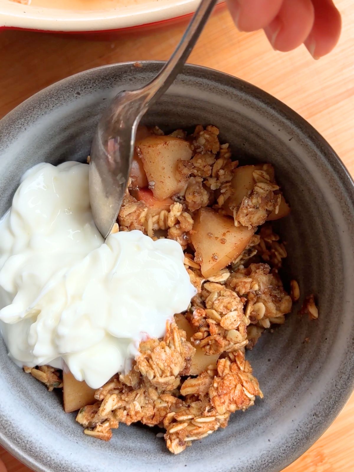 Spoon taking a bite from a bowl of apple crisp.