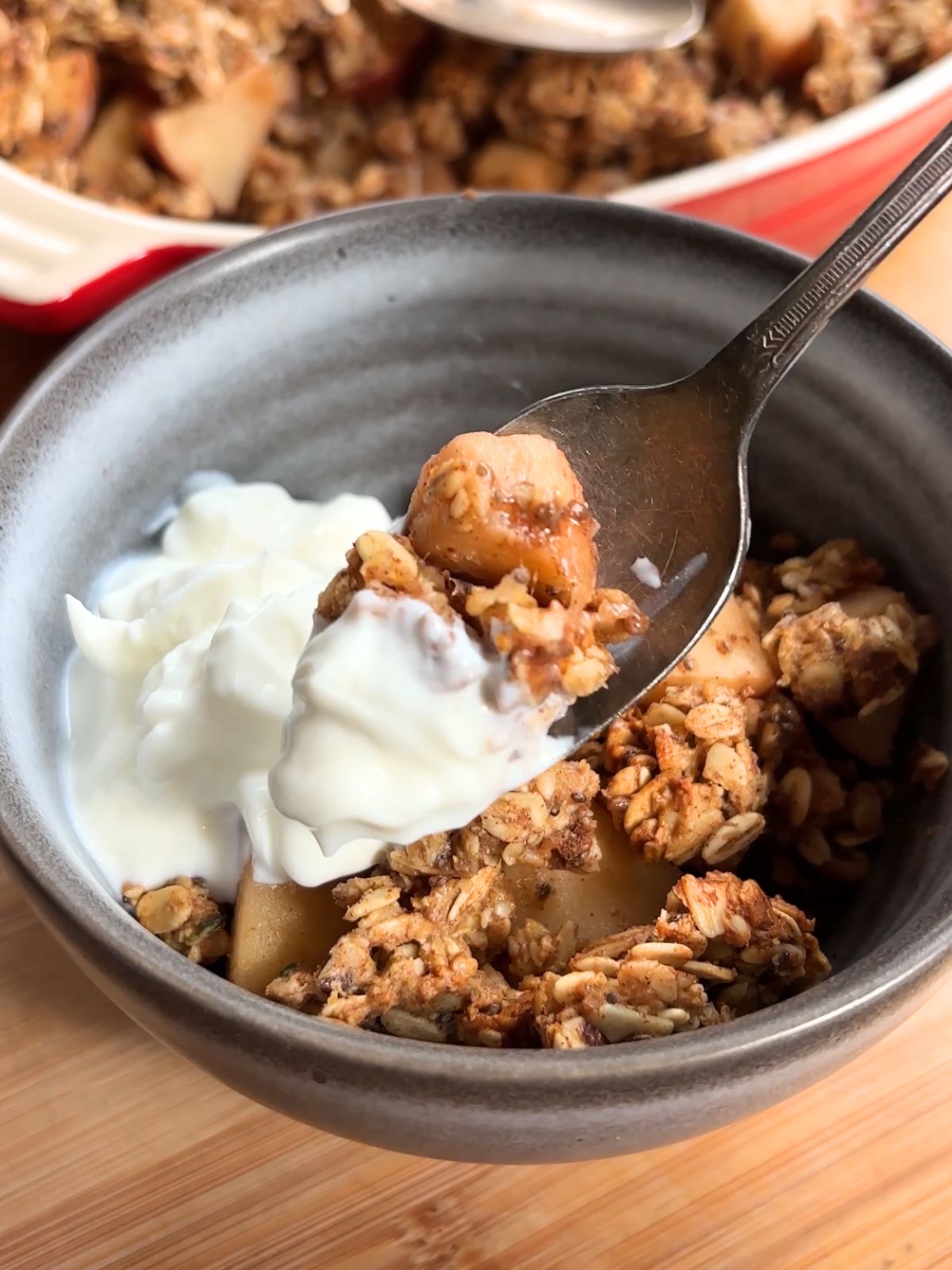 Spoon holding up apples with granola topping and yogurt.
