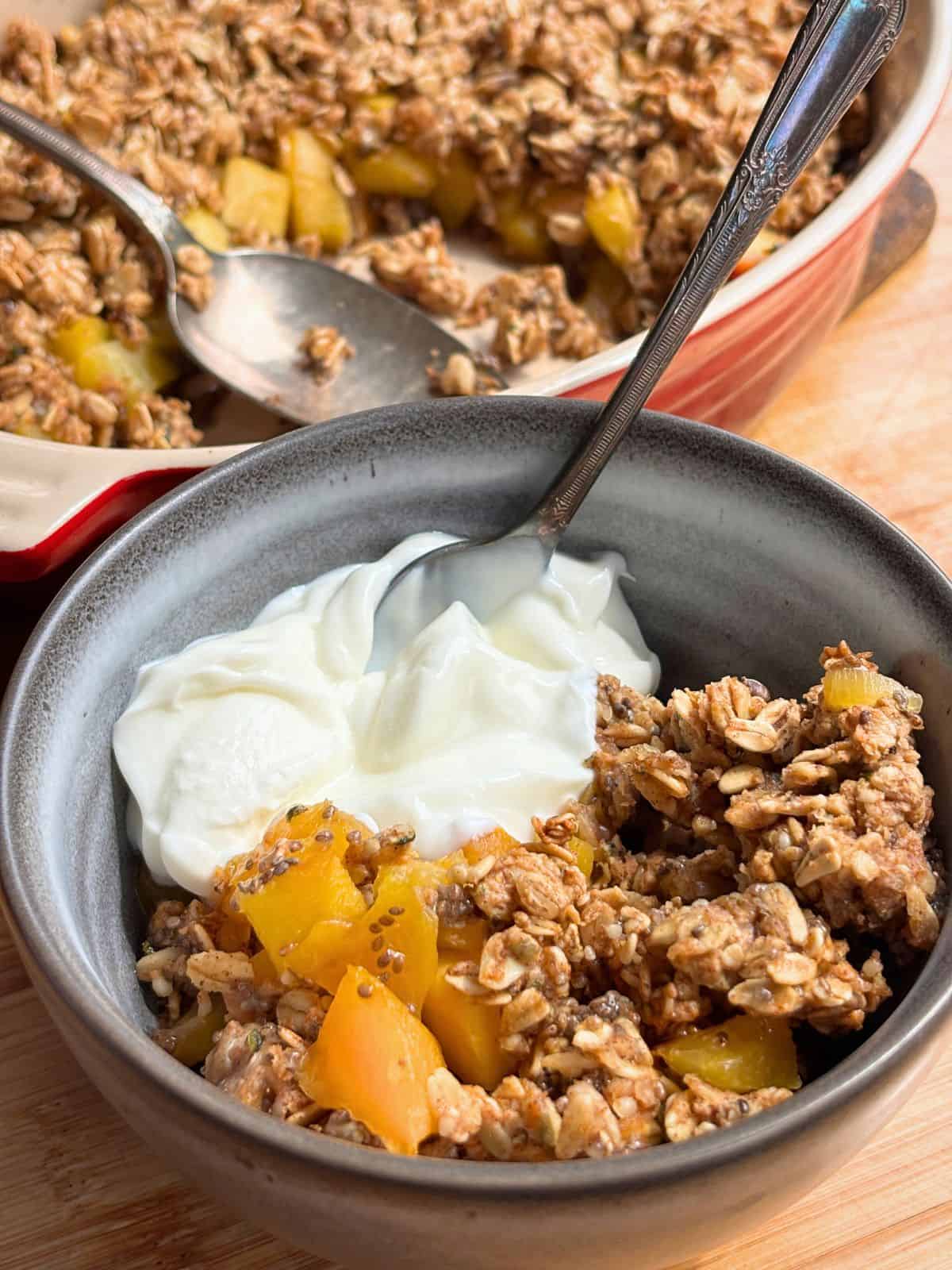 Spoon in a bowl of breakfast peach crisp.