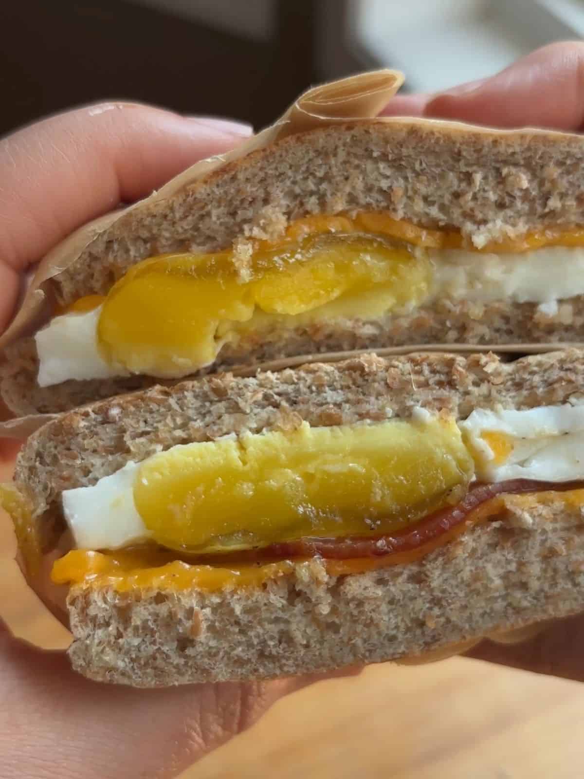 Hand holding a breakfast sandwich sliced in half.