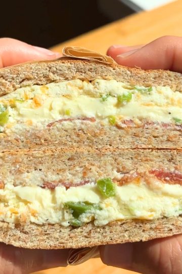 Hand holding a breakfast sandwich sliced in half.
