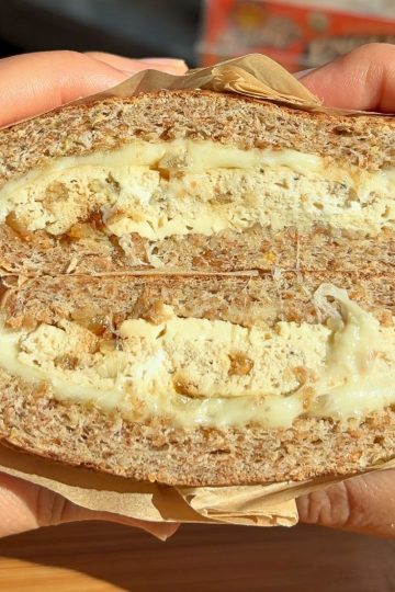 Hand holding a sliced French onion breakfast sandwich.